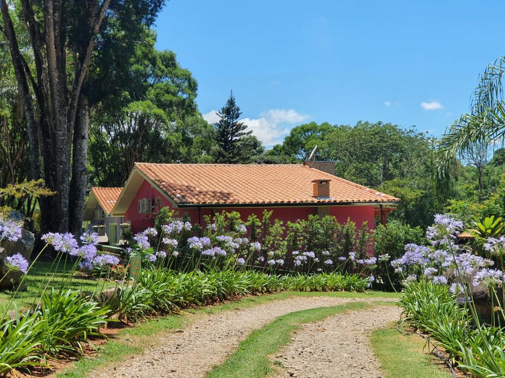 a red house with a garden with purple flowers at Pousada Villa das Águas,chalés com Ar condicionado e um rio no quintal in Monte Alegre do Sul