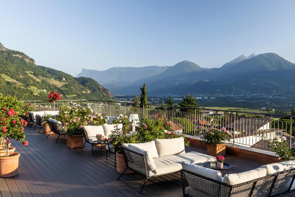 un balcón con sofás, flores y montañas en Hotel Pienzenau Am Schlosspark, en Merano