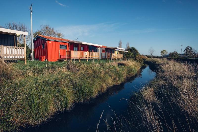 um comboio vermelho está estacionado ao lado de um rio em Camping du Lac de Saujon em Saujon