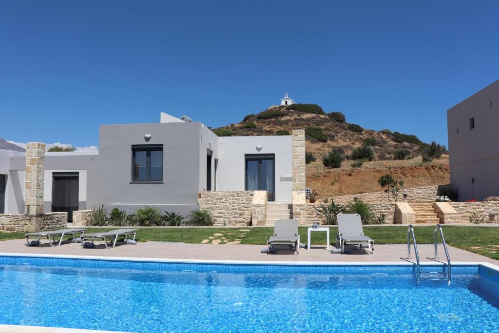 a swimming pool with two chairs and a house at TRIOPETRA VIEW 3 in Triopetra