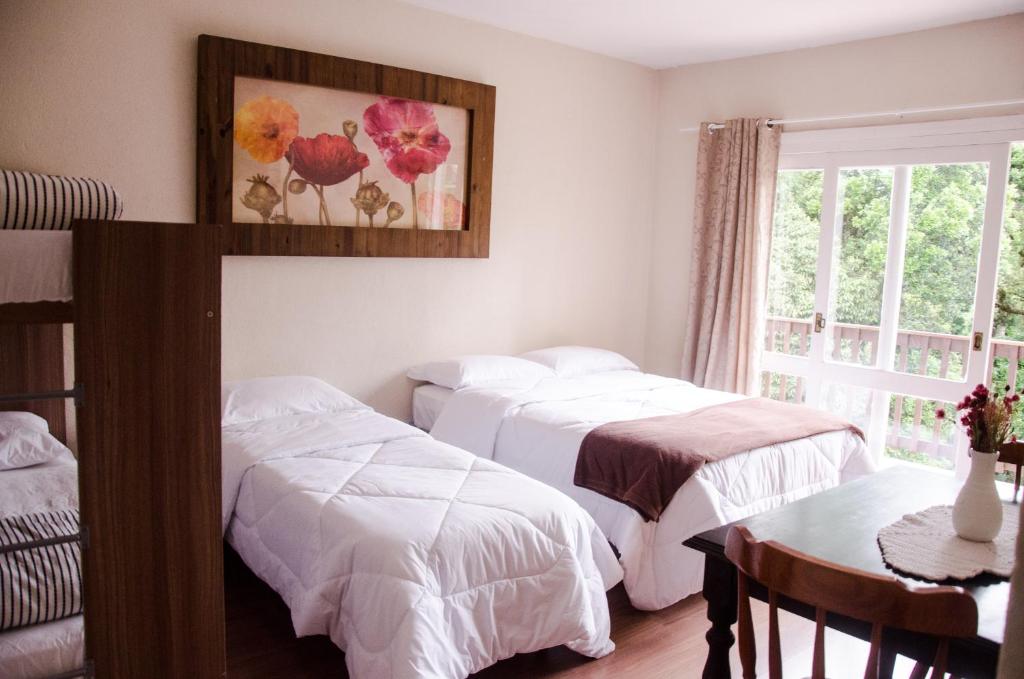 a bedroom with two beds and a table and a window at Residenciais Belo Centro Gramado in Gramado