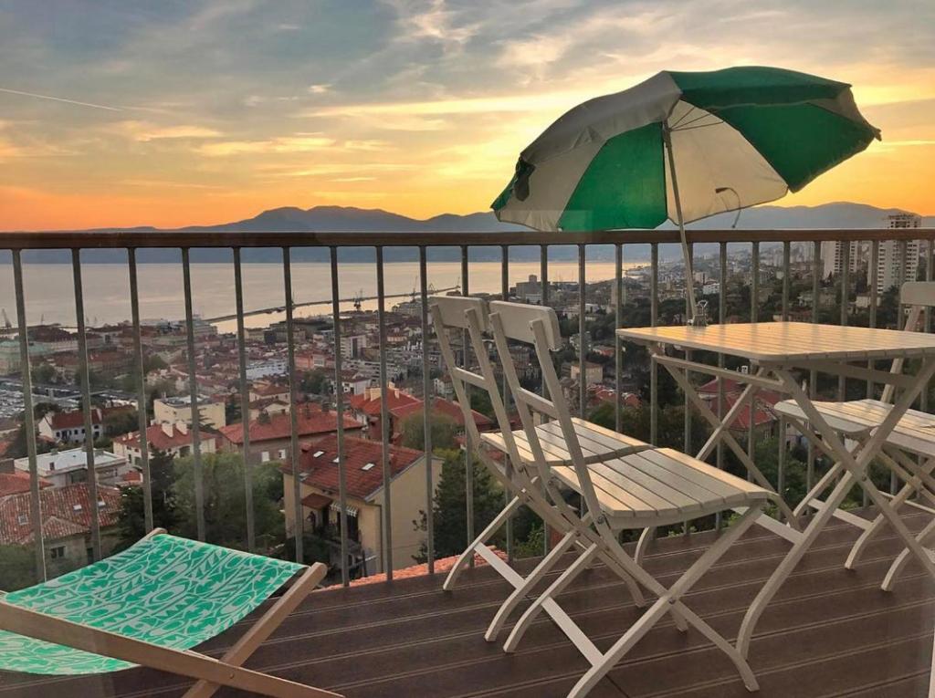 ein Tisch und zwei Stühle und ein Sonnenschirm auf dem Balkon in der Unterkunft Linden Trsat with balcony in Rijeka