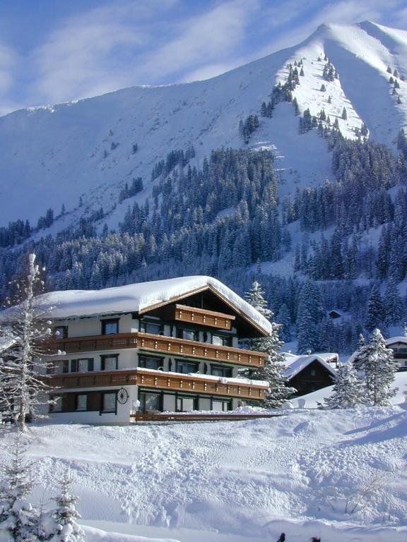 a building in the snow in front of a mountain at Gästehaus Etschmann in Riezlern