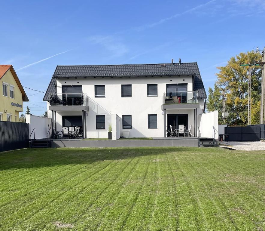 a white house with a large yard in front of it at Bala-Home Apartmanok in Balatonboglár