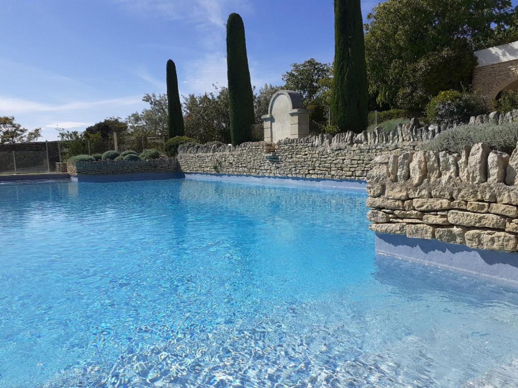 una piscina de agua azul y una pared de piedra en Le Mazet Du Domaine, en Gordes