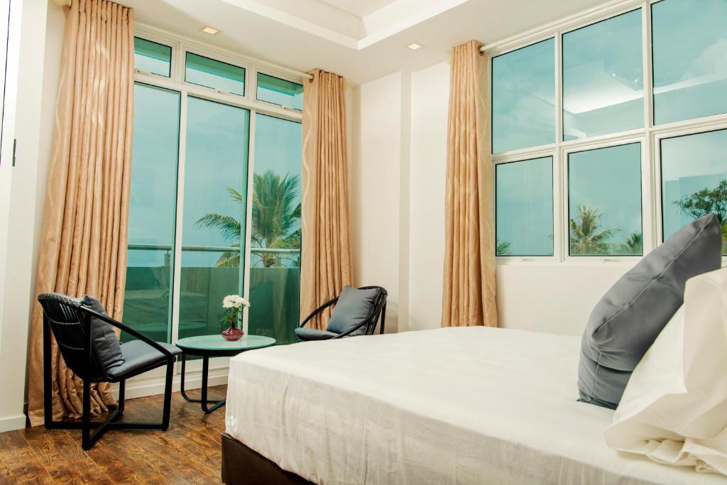 a bedroom with a large bed and chairs and windows at Acacia Beach Hotel in Hulhumale