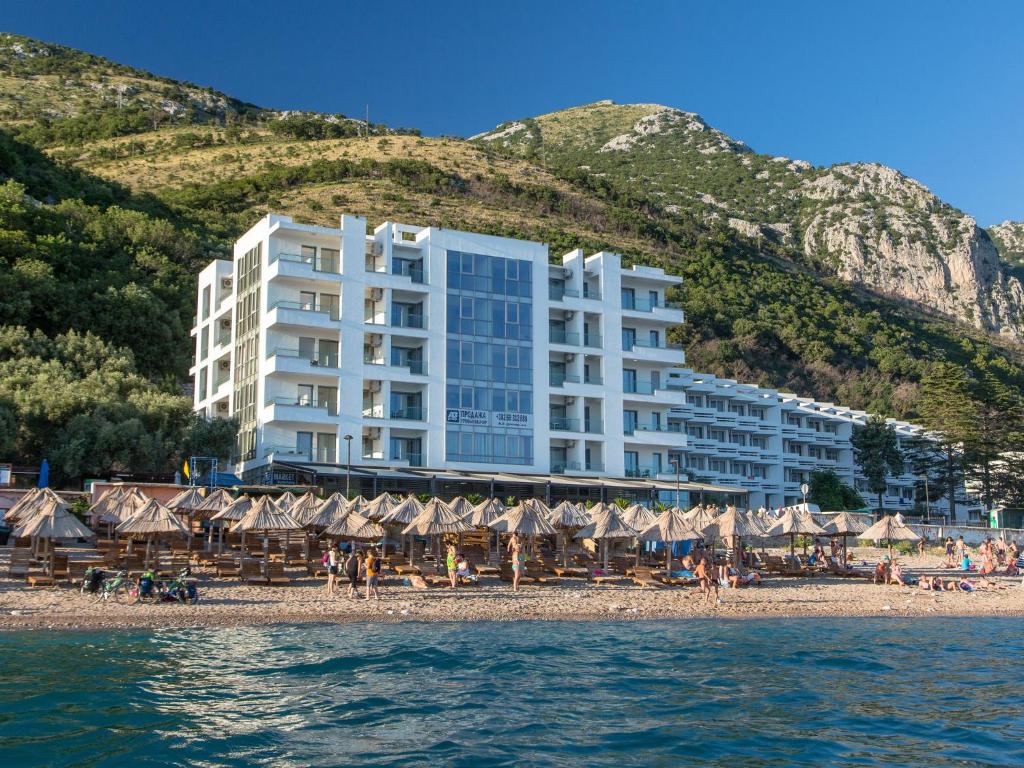 a hotel on a beach with umbrellas and people on the beach at Apart Hotel Sea Fort in Sutomore