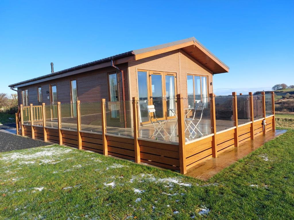 ein winziges Haus mit einer Terrasse auf dem Rasen in der Unterkunft Luxury family Beechwood lodge with hot tub in Lochwinnoch