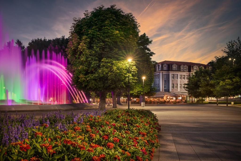 a fountain in a park with a building and flowers at Hotel Splendid in Pleven