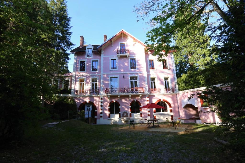 Una gran casa rosa con mesas delante. en Hotel La Font Vineuse & Spa, en Saint-Pierre-dʼArgençon