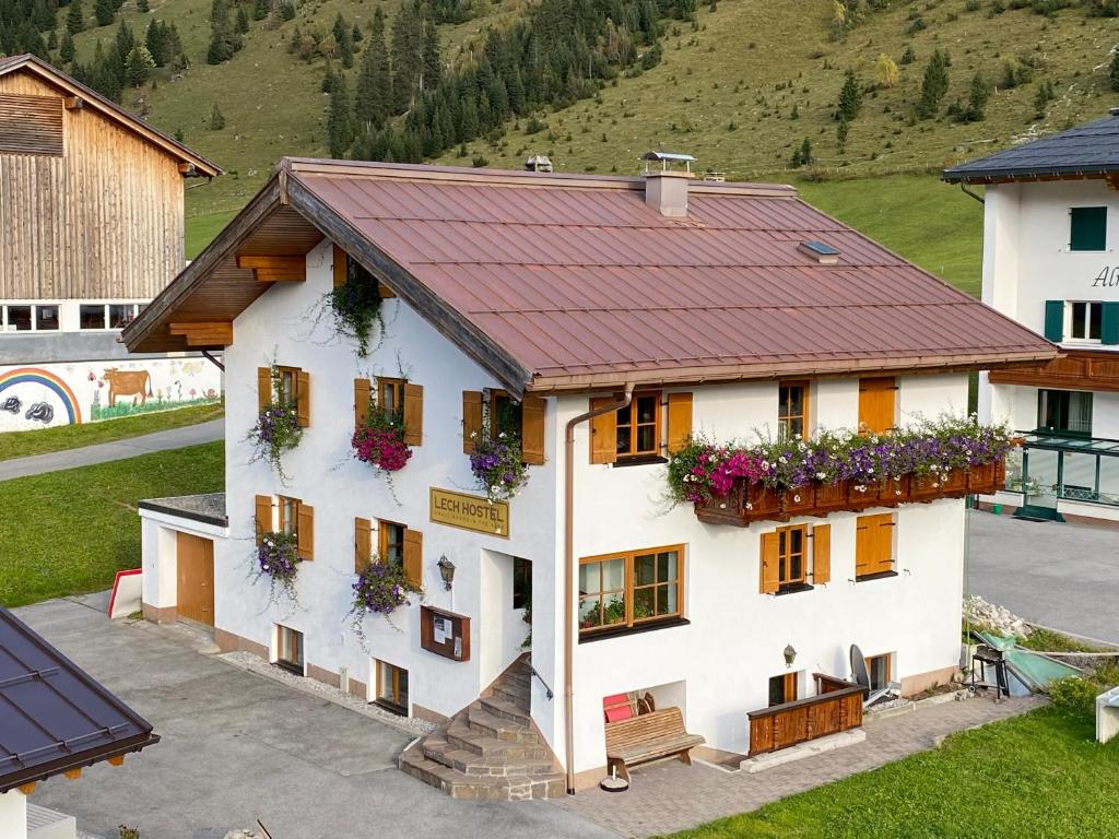 a white house with a red roof and flowers on the windows at Lech Hostel in Lech am Arlberg