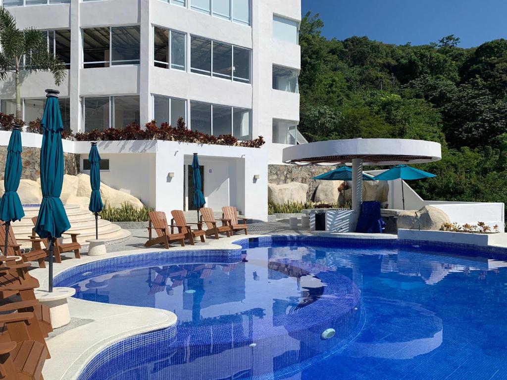 uma piscina com cadeiras e guarda-sóis ao lado de um edifício em La Villa de Almudena em Acapulco