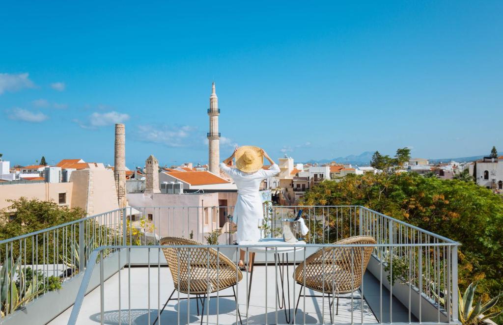a woman standing on a balcony with a table and chairs at Neratze Hammam Suites in Rethymno