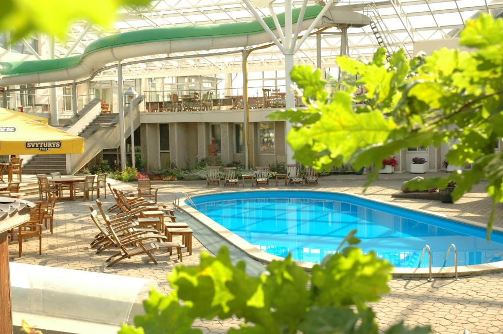 a swimming pool with tables and chairs and a building at Ąžuolynas in Juodkrantė