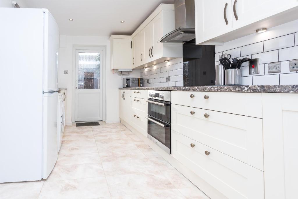 a white kitchen with white cabinets and a refrigerator at The White & Warm, Free Parking & Wifi, 8 beds in Colchester