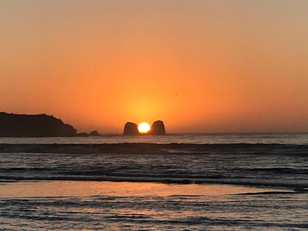 un coucher de soleil sur l'océan avec deux grandes formations rocheuses dans l'établissement Esfera Pichilemu - Lodge, à Pichilemu