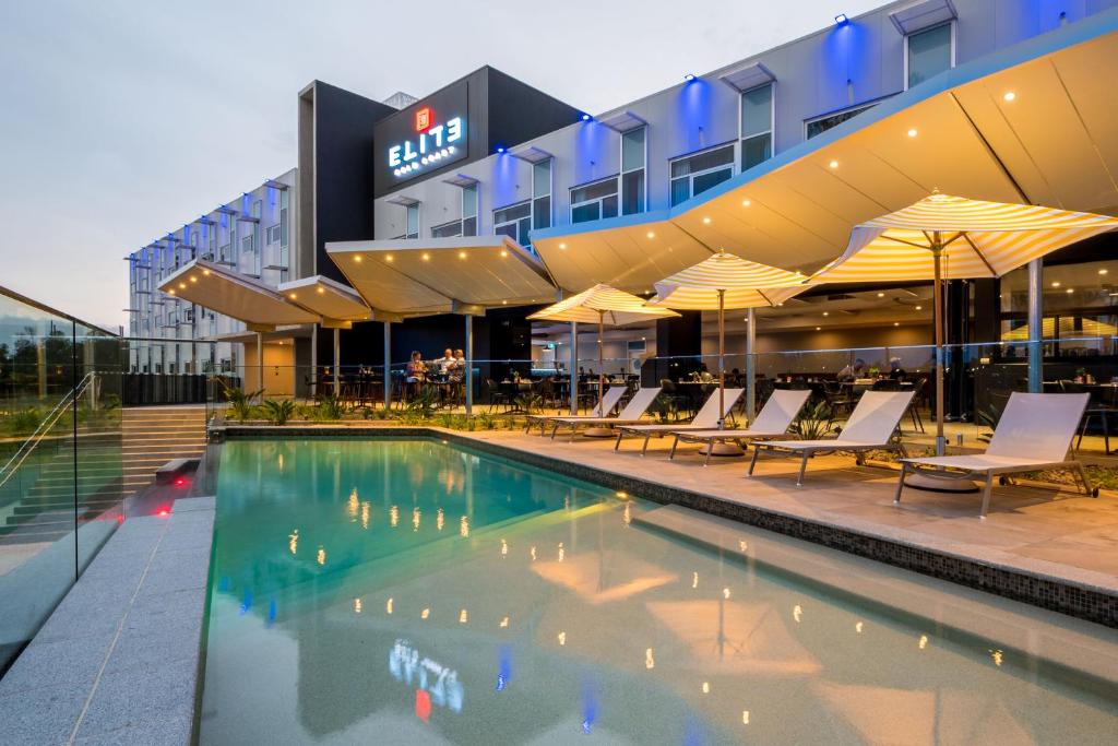 a hotel pool with chairs and umbrellas in front of a building at Elite Gold Coast in Gold Coast