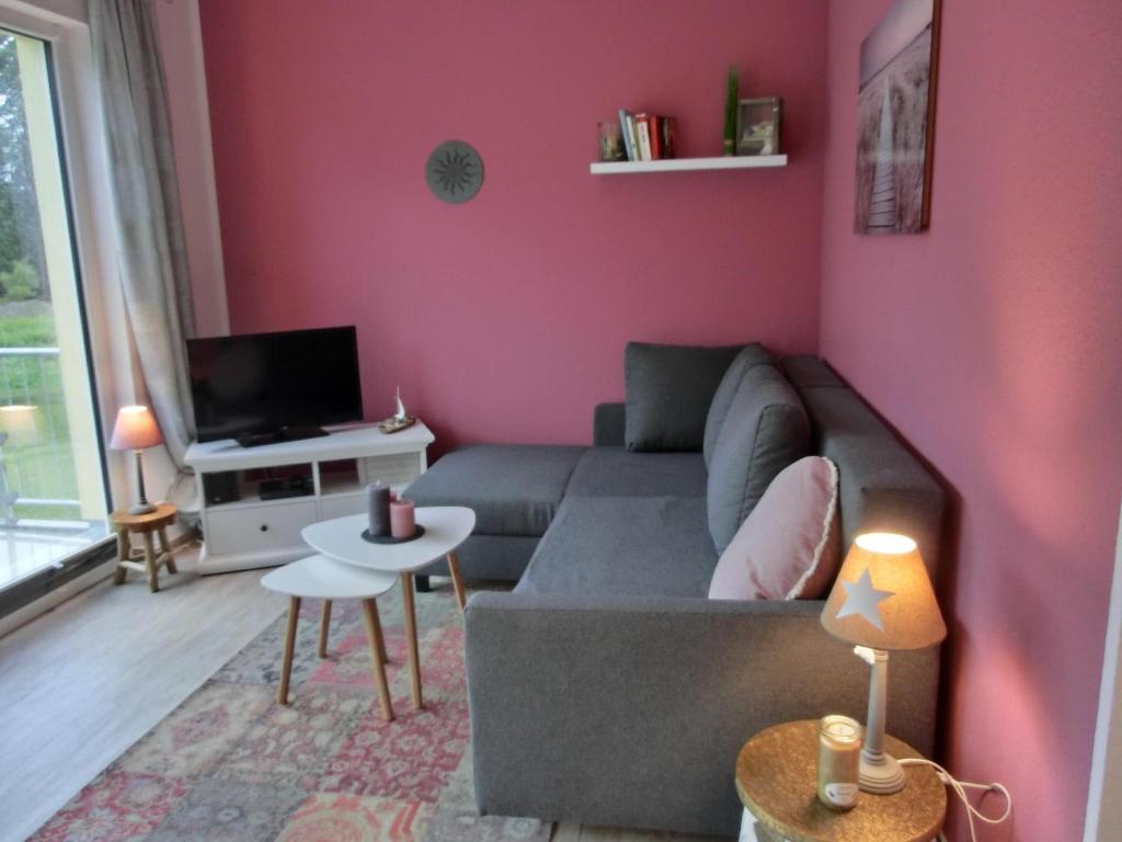 - un salon avec un canapé gris et un mur rose dans l'établissement Ferienwohnung KWi 17 OG "Küsten-Koje", à Graal-Müritz