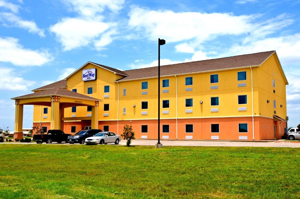 a large yellow building with cars parked in a parking lot at Best Way Inn Cleburne in Cleburne