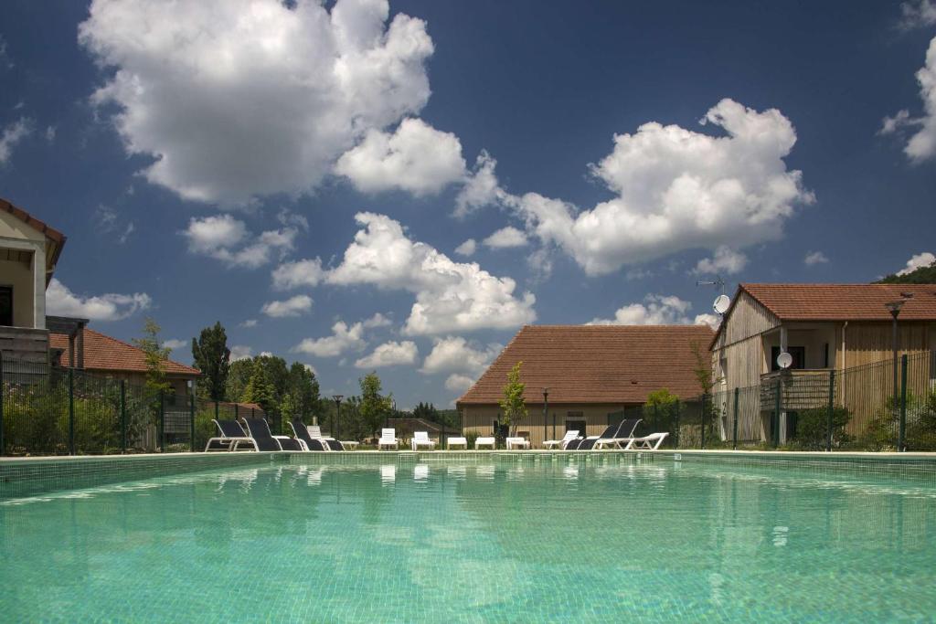 a swimming pool with chairs and a sky with clouds at Vacancéole - Résidence Le Clos du Rocher in Les Eyzies-de-Tayac
