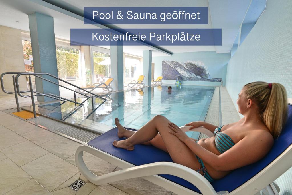 a woman in a bathing suit sitting on a chair in a swimming pool at Hotel Apollo Garni in Regensburg