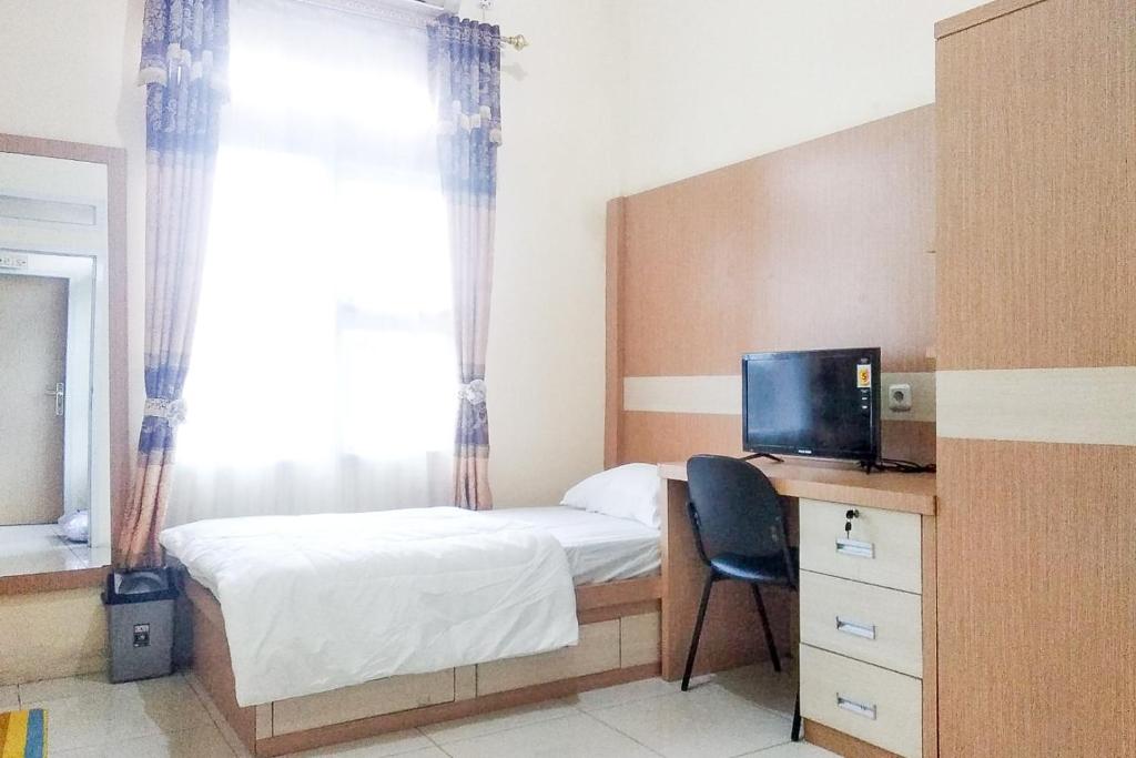 a bedroom with a bed and a desk with a television at Griya De Riz Syariah Mitra RedDoorz in Jambi