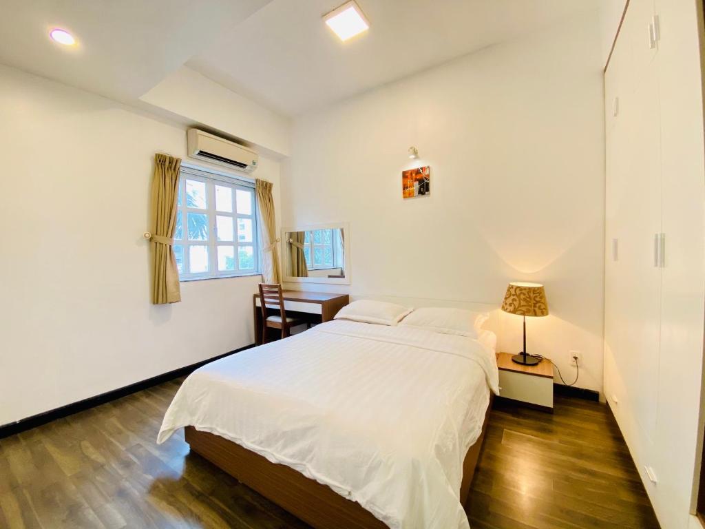 a white bedroom with a bed and a desk at Pearl Service Apartment in Ho Chi Minh City