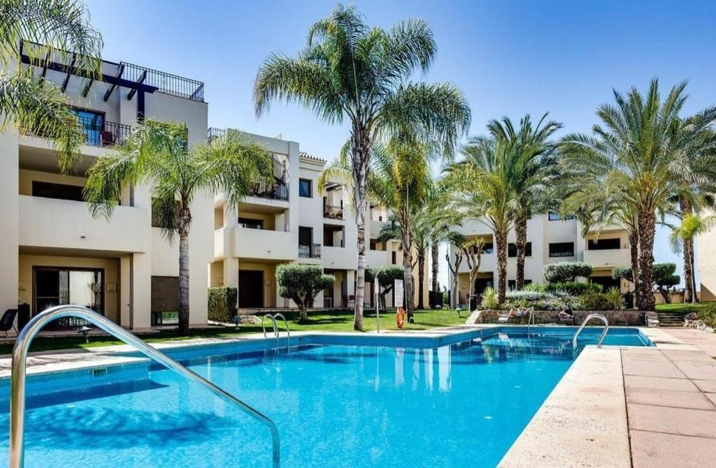 una piscina frente a un edificio con palmeras en Roda Golf Resort FIT FOX, en Murcia