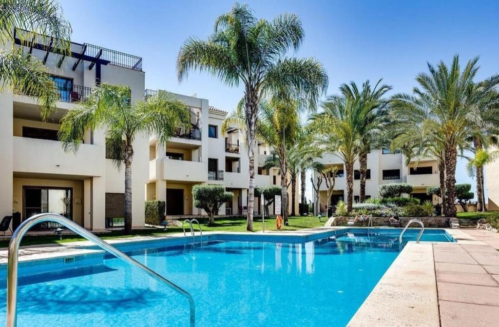 a swimming pool in front of a building with palm trees at Roda Golf Resort FIT FOX in Murcia