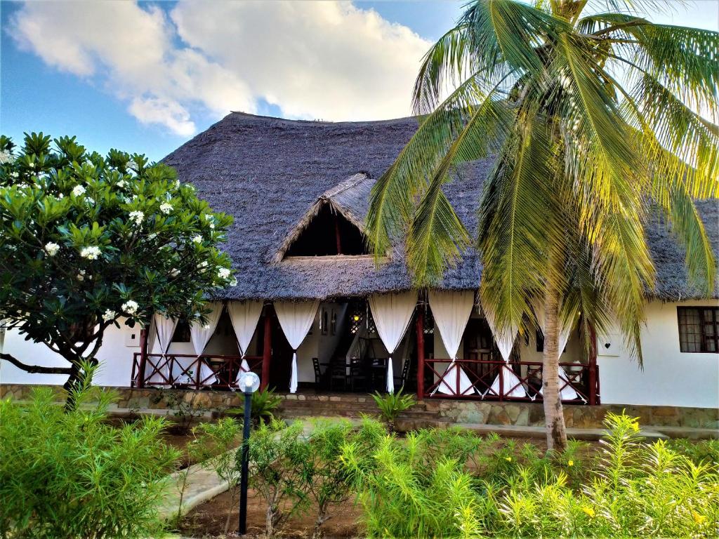 una casa con techo de paja y una palmera en Karibuni Jeds Villas 85 & 86 en Mambrui