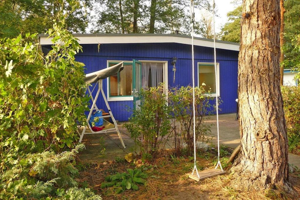 una casa azul con un patio de juegos delante de ella en Bungalow am Groß Labenzer See Klein Labenz - DMS01035-B, en Klein Labenz