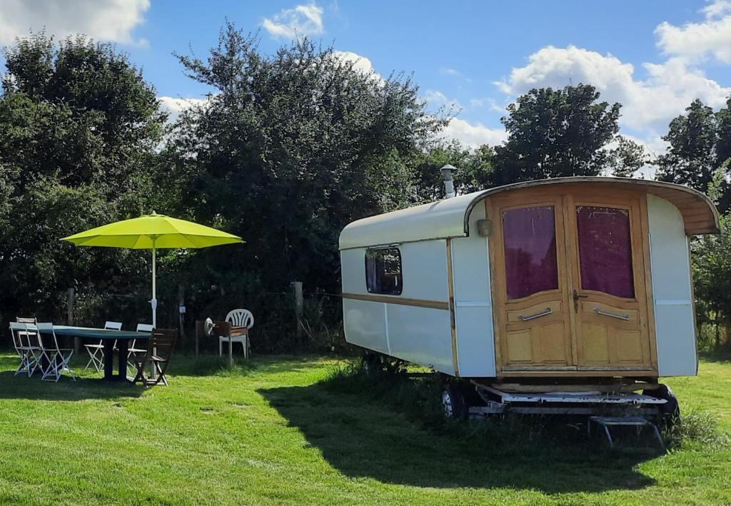 a white trailer with a table and an umbrella at Manoir du Bois Joly - Roulotte Gitane in Margon