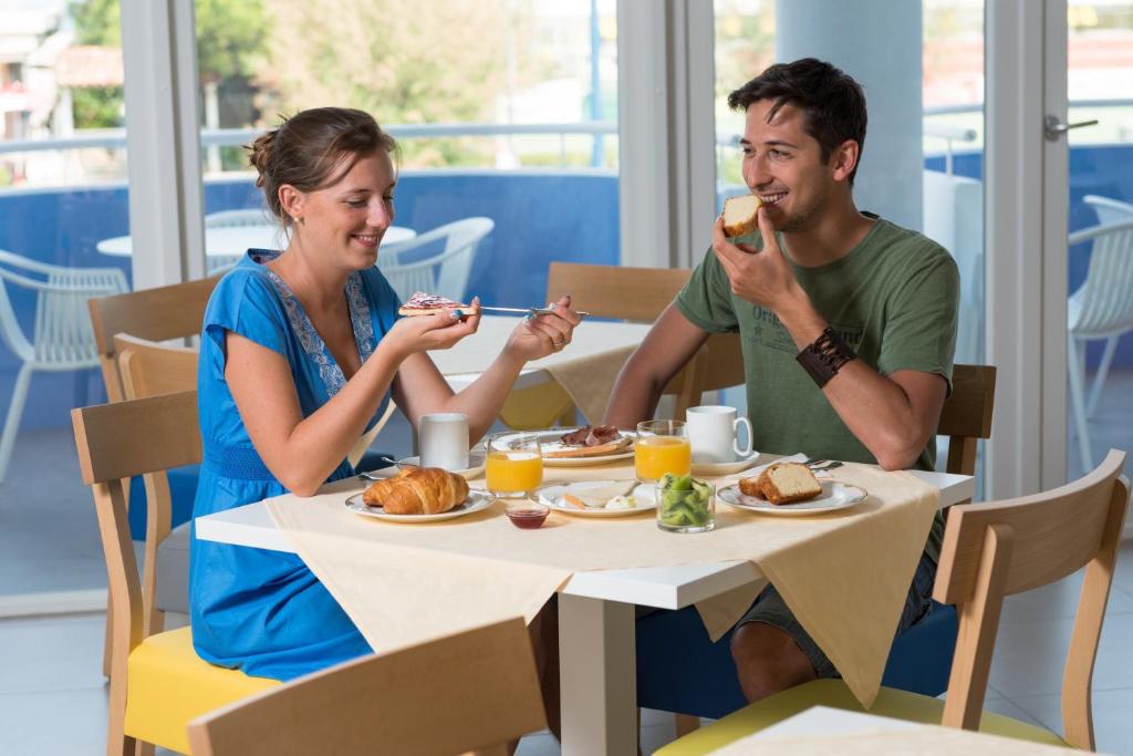 a man and a woman sitting at a table eating food at Hotel Mediterraneo in Sottomarina