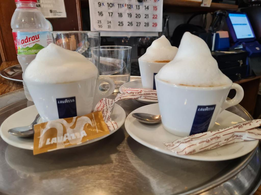 two cups of coffee sitting on a table with plates at Hostal S'Algaret in Fornells