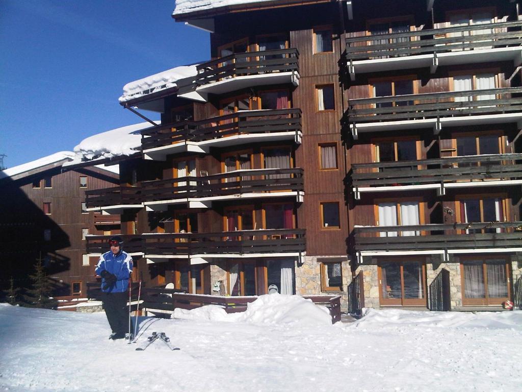 un homme debout dans la neige devant un bâtiment dans l'établissement Ski in and Out 2-Bed Apartment in Meribel, à Les Allues