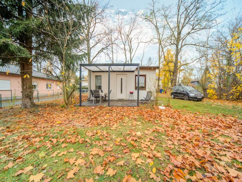 una pequeña casa en un patio con hojas en el suelo en Holiday home with garden in Mahlow Brandenburg, en Mahlow
