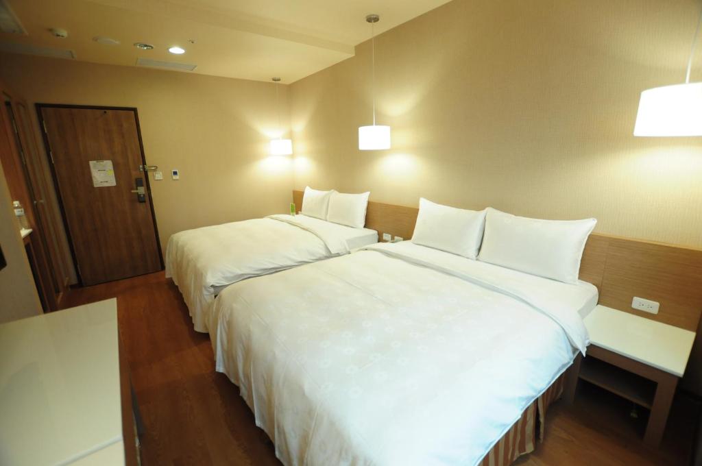 two beds in a hotel room with white sheets at Kindness Hotel - Kaohsiung Main Station in Kaohsiung