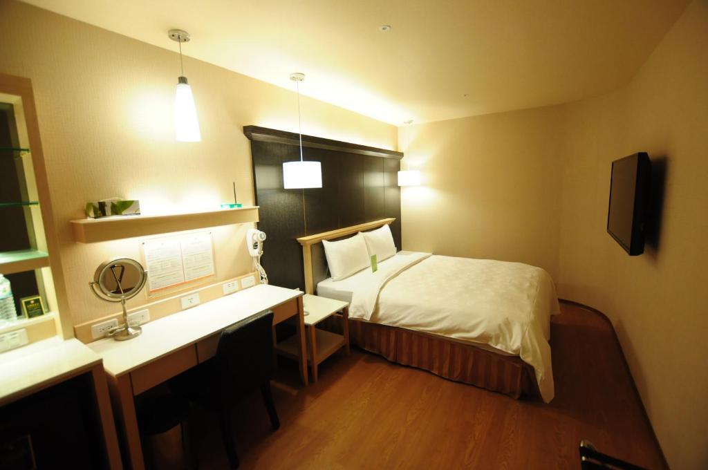 a bedroom with a bed and a desk with a mirror at Kindness Hotel - Kaohsiung Main Station in Kaohsiung