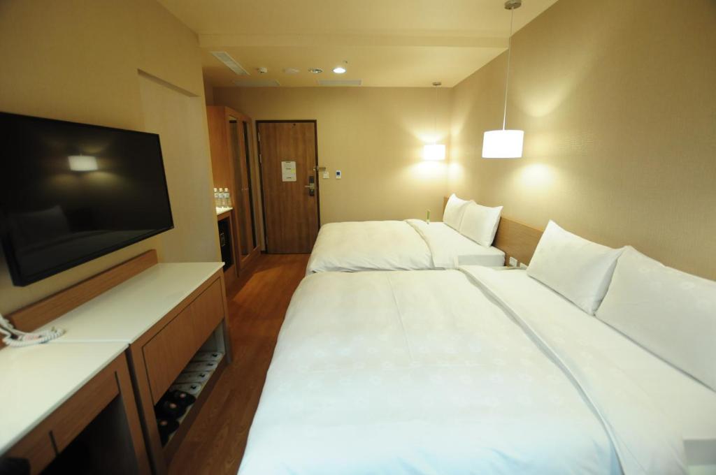 a hotel room with two beds and a flat screen tv at Kindness Hotel - Kaohsiung Main Station in Kaohsiung