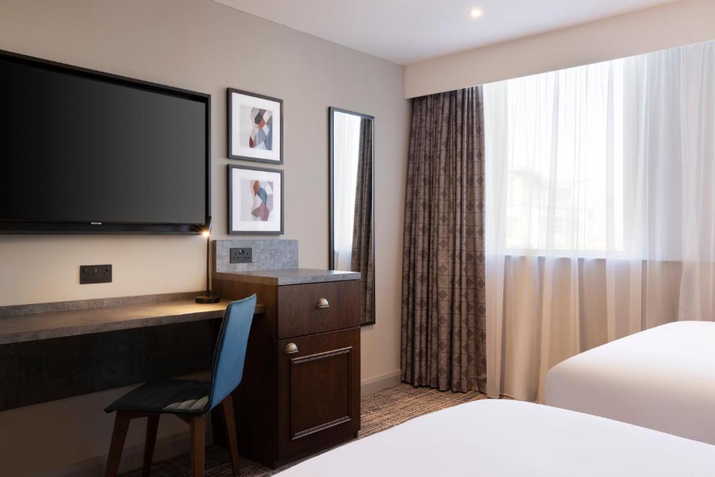 a hotel room with a desk with a television and a bed at Leonardo Royal Hotel Birmingham in Birmingham