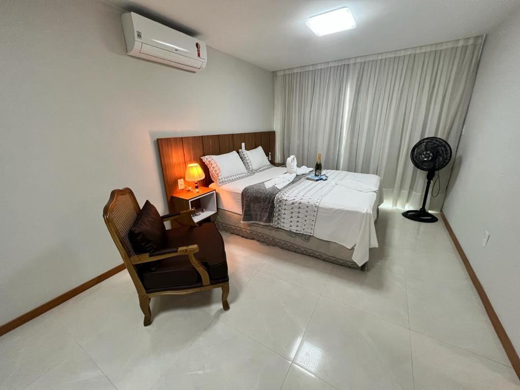 um quarto com uma cama, uma cadeira e uma ventoinha em Magnífico APARTAMENTO de Charme - 3 quartos AR CONDICIONADOS SPLIT - Beira Mar, 2 banheiros, 2 vagas garagem, 4 varandas, 2 elevadores, Redes para descanso, Wi-Fi, Air Fryer, Disney Plus, Star Plus, HBO Max, Guarda Sol, Cadeiras de Praia e Caixa Térmica em Guarapari