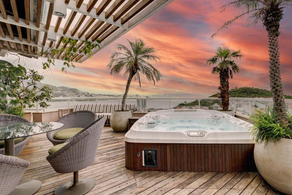 a jacuzzi tub on a deck with palm trees at Triplex com jacuzzi na melhor vista de Floripa! in Florianópolis