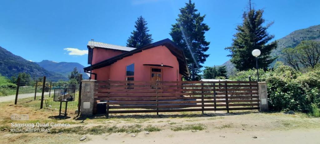 a small red house with a fence and mountains in the background at Zonda hostel cultural in Lago Puelo