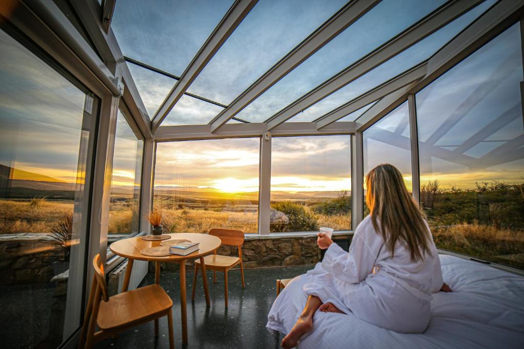 une femme assise au lit devant une fenêtre dans l'établissement SkyScape, à Twizel