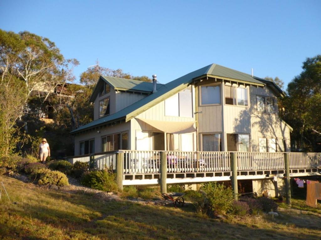 a house on a hill with a person standing in front of it at Snowgums on the Lake - Charming 4BR Home l Amazing Lake Views l Balcony in Jindabyne