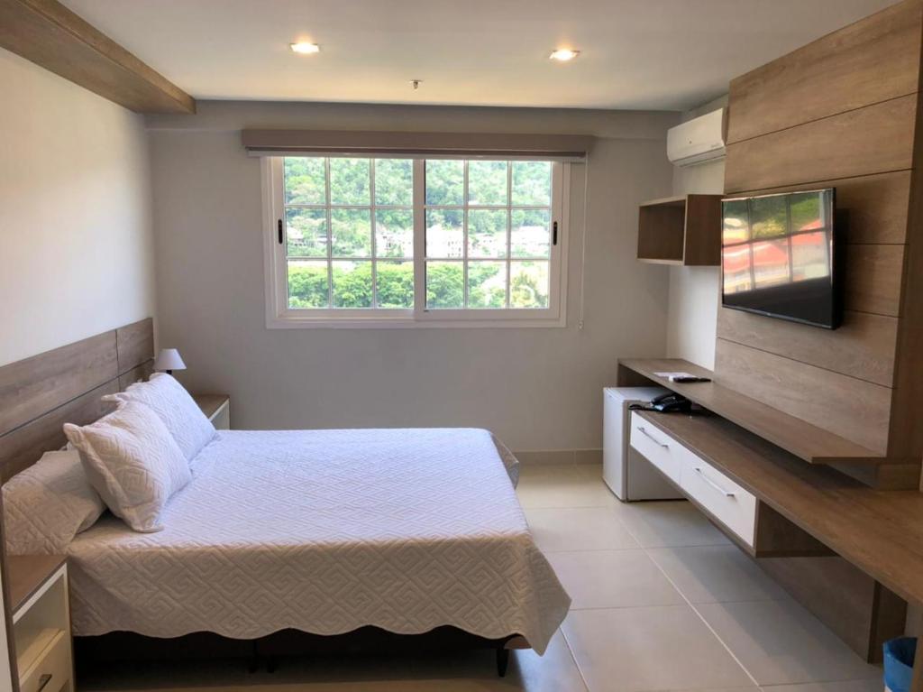 sypialnia z łóżkiem, telewizorem i oknem w obiekcie Live Suites Itaipava w mieście Itaipava