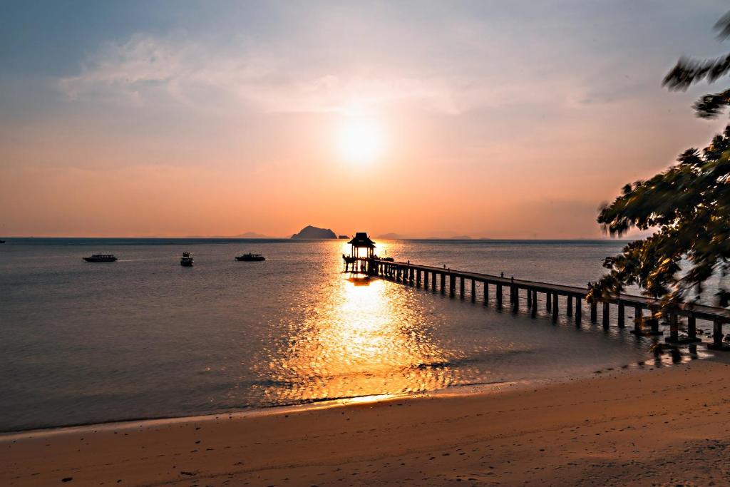 eine Person, die auf einem Pier am Strand bei Sonnenuntergang steht in der Unterkunft Santhiya Koh Yao Yai Resort & Spa - Compulsory Join Santhiya Speedboat from-to Ao Po Grand Marina at Phuket in Ko Yao Yai