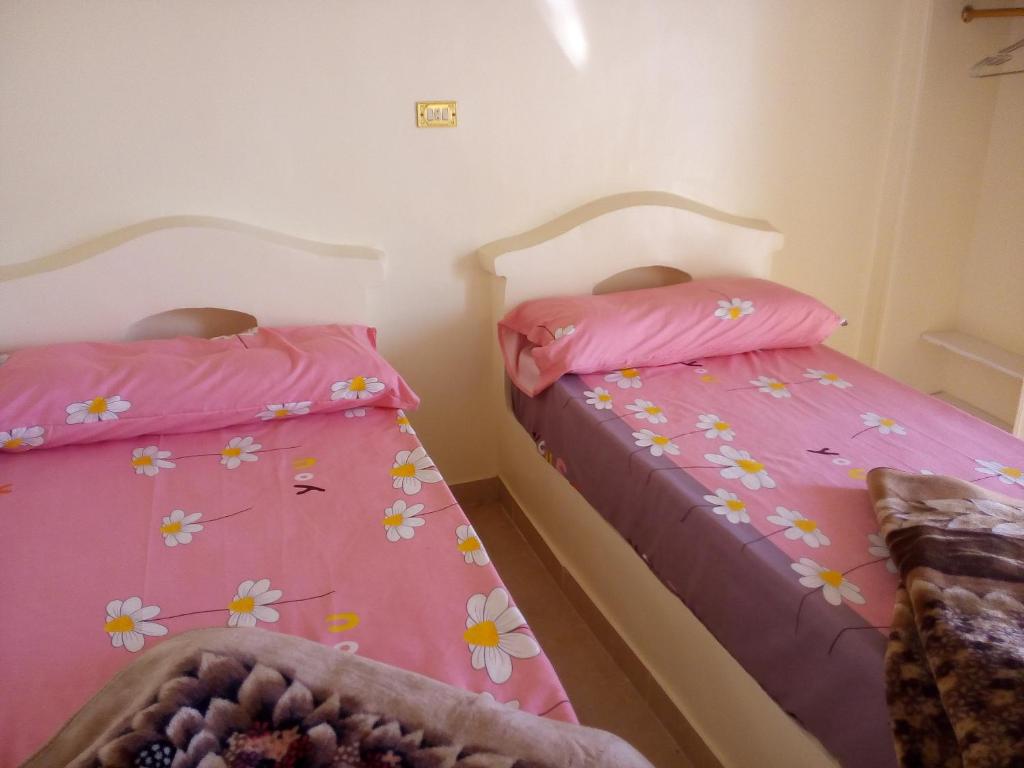 two beds in a bedroom with pink sheets and flowers at Roma House in Aswan