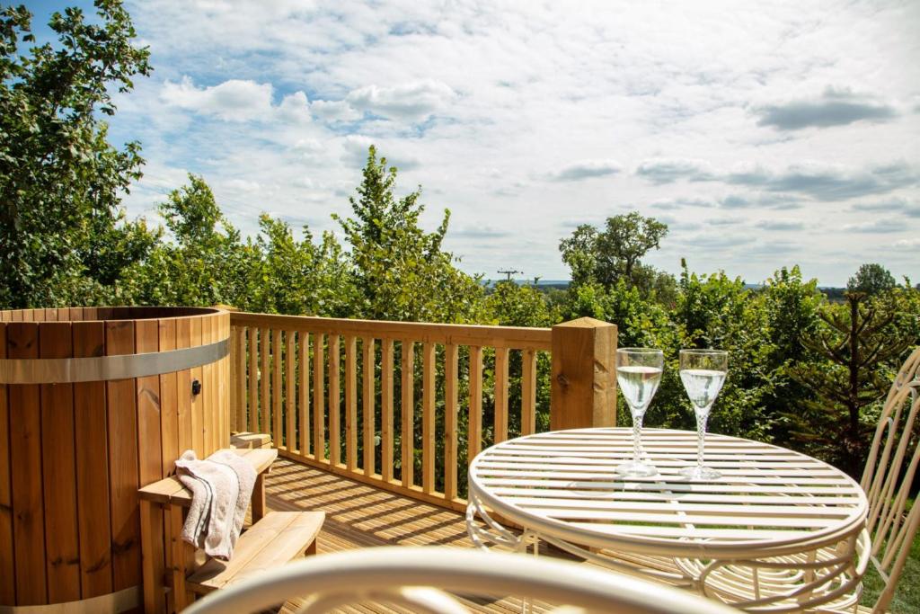 a wooden deck with a table and two wine glasses at Abbey Farm Glamping & Cottage in Thame