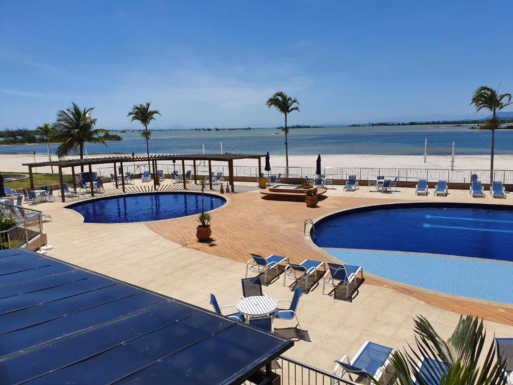 un complejo con piscina, sillas y playa en Flat Golden lake, en Arraial do Cabo